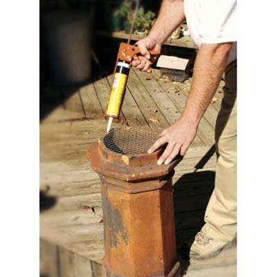 a man cuts and adheres a small piece of metal screen to the top of the chimney pot