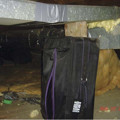 luggage and a brick supporting an HVAC duct in a crawlspace