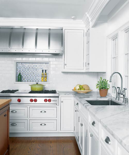 kitchen after remodel with white cabinetry, pale-marble countertops, studded steel range hood