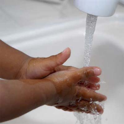child washing his or her hands under a sink faucet