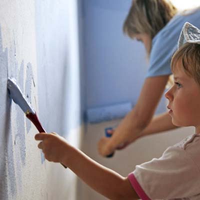 child painting a wall blue with adult supervision