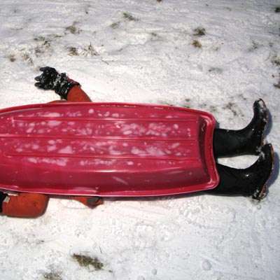 child laying under sled in snow