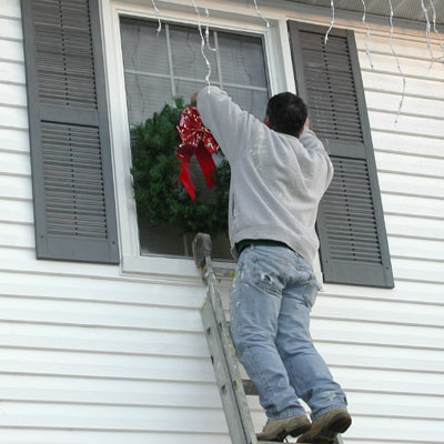 man on ladder decorating exterior of house for holidays