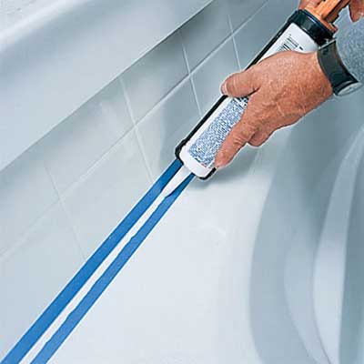 hands applying caulk between a bathtub and tile
