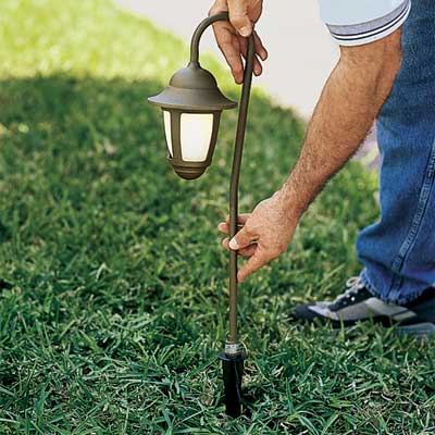 hands pushing a yard light fixture into the ground