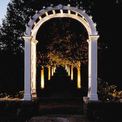 a tree-lined path with a pergola lit up at night