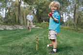 small child playing croquet in yard