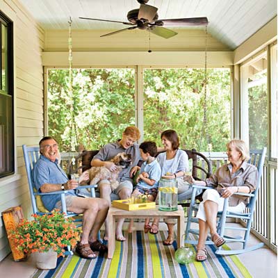 family sitting on porch swing, chairs on remodeled bungalow 