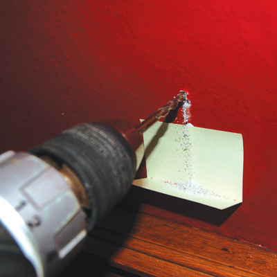 drilling hole in wall with sticky note underneath to catch the dust