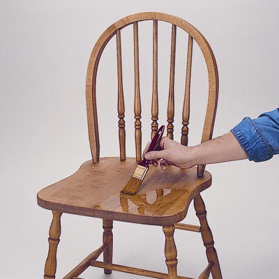 man applies polyurethane to a chair seat using a brush