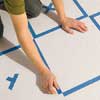 smoothing painter's tape on a wood floor to complete a checkerboard outline