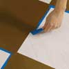 removing the painter's tape from a checkerboard-painted wood floor