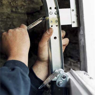 hands holding the wrench tightening the bolts of the garage door's upper tracks
