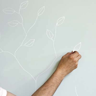 hand shown sketching branches with leaves on a wall with chalk