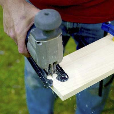 hands using a jigsaw to cut a wood board to cut the curve into the legs of the pet ramp