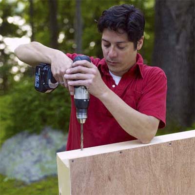 man using a drill driver to drill holes for the leg bolts