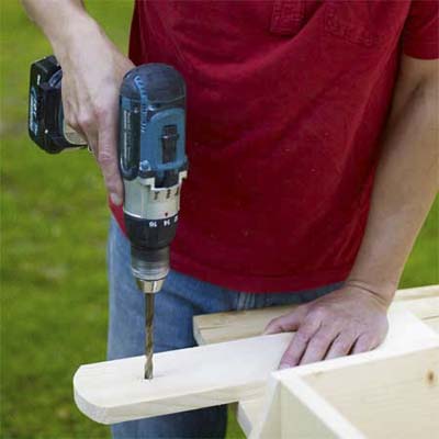 man using a drill driver to drill bolt holes in the legs