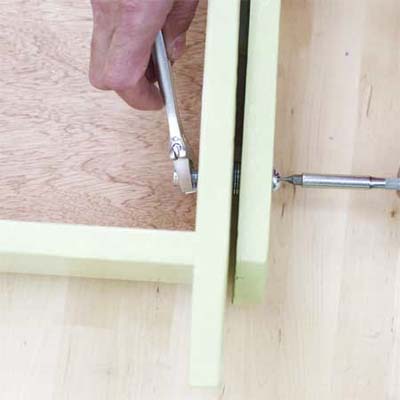 hands using an adjustable wrench and screwdriver to bolt the legs to the box