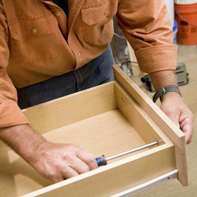 Tom Silva attaching knobs to the drawer fronts of the joined cabinets