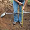 man with tape measure checking the depth of a hole by measuring from the shovel handle laid across the hole