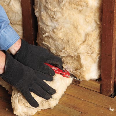 man cutting insulation batting to fit wall cavity