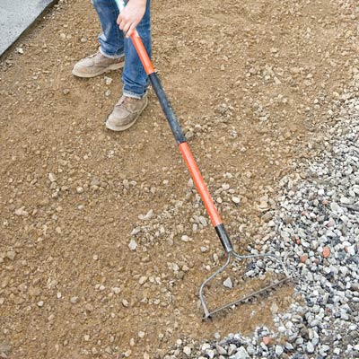 raking leveling sand into an area of removed driveway