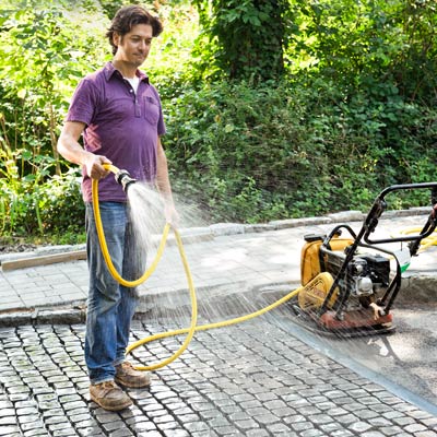 spraying a cobblestone driveway apron with water to prevent grout from sticking to the top