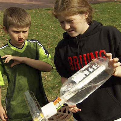 boy looks on as girl loads a bottle onto the PVC tubing filled a third of the way with water