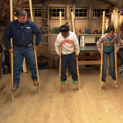 man and children walking on hand made wooden stilts